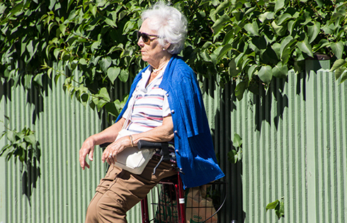 Äldre kvinna med solglasögon sitter på sin rollator i solen.