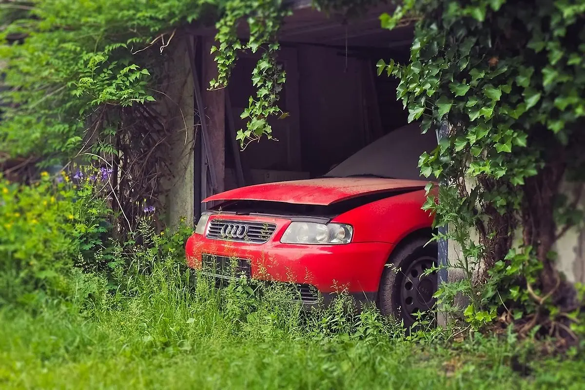 Röd skrotbil i en enklare garagebyggnad