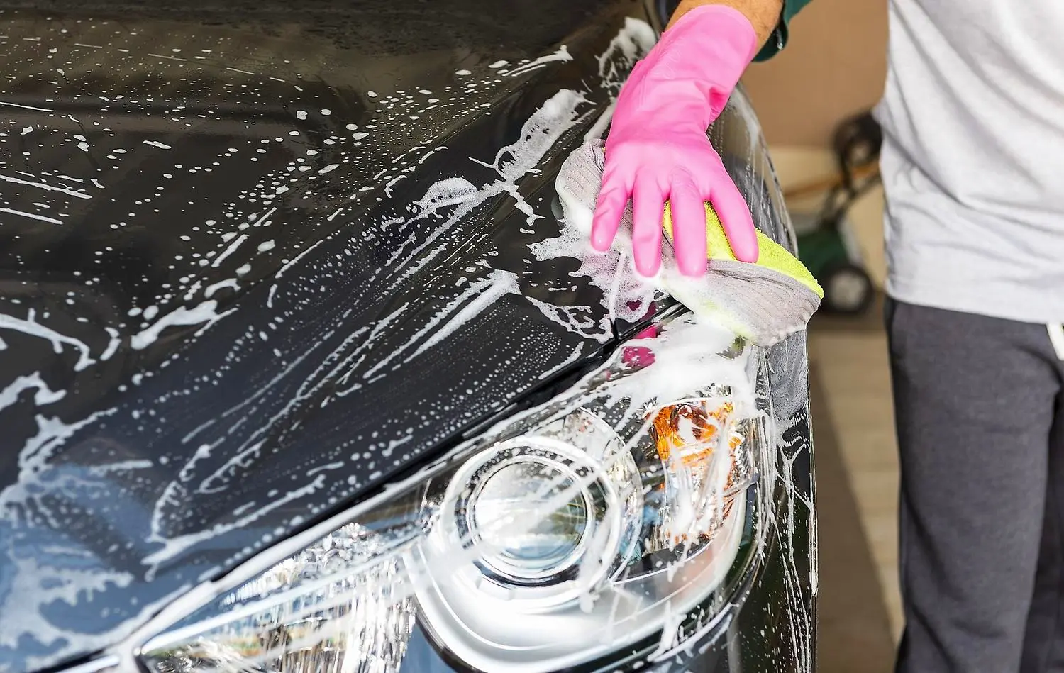 Person tvättar bilen med skummande svamp och rosa plasthandske 