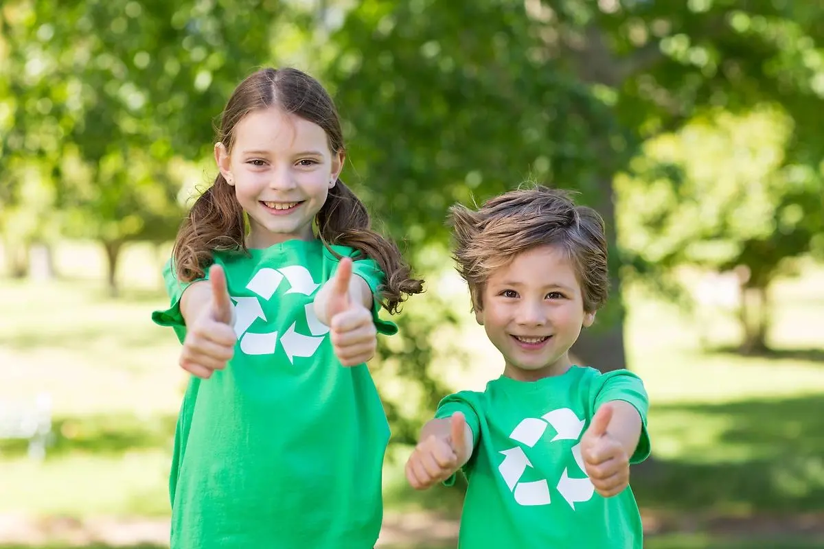 Flicka och pojke i gröna tröjor gör tummen upp till återvinning