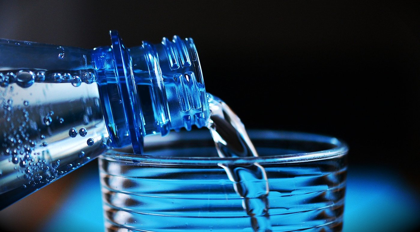 En blå bild där man häller upp vatten från en flaska i ett glas.