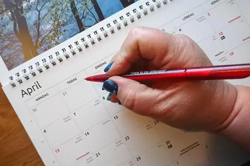 Hand skriver i en almanacka med röd penna 