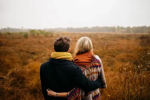 Två personer med armarna om varandra framför ett höstlikt landskap