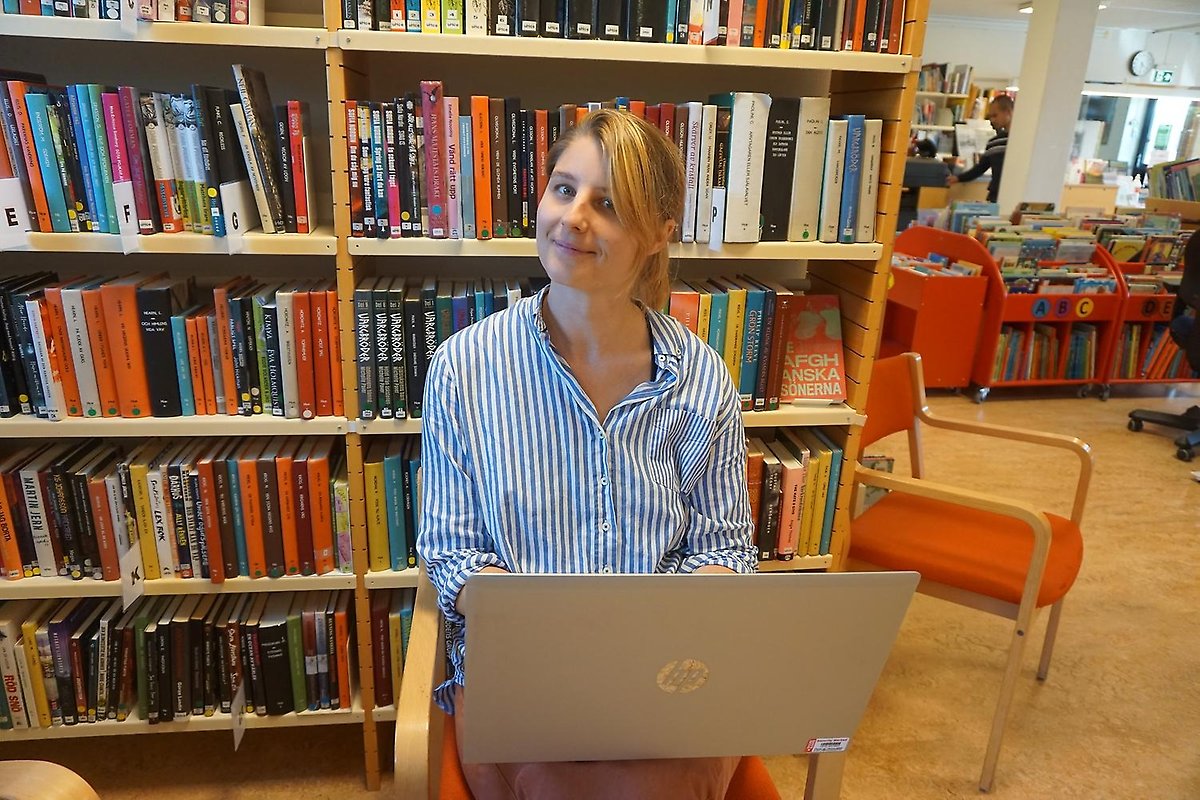 Caroline Wänblad sitter framför bokhylla i Östervåla bibliotek