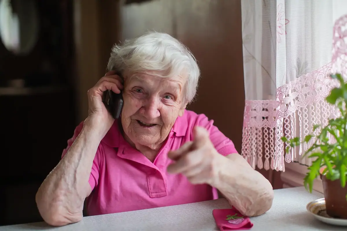Äldre kvinna vid ett fönsterbord pratar i telefon 