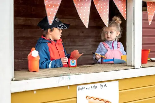 Två förskolebarn leker utomhus i en låtsaskiosk